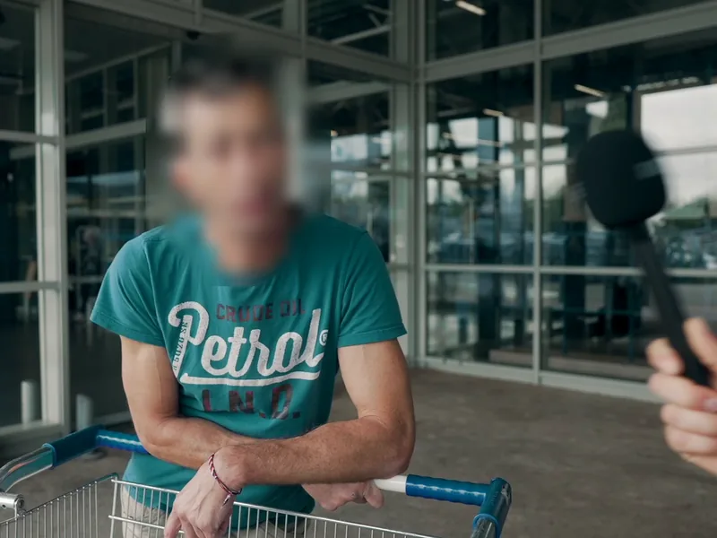 Un client, appuyé sur son chariot, répond à une interview à la sortie d'un magasin. Son visage est flouté.